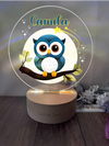 a glass night light with an owl sitting on a branch